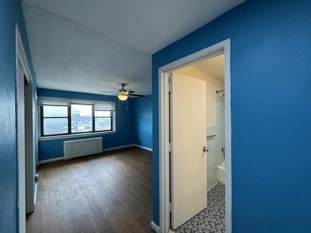 unfurnished bedroom featuring a ceiling fan, radiator heating unit, baseboards, and wood finished floors