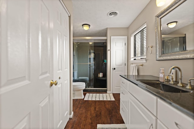 bathroom with toilet, visible vents, a stall shower, and wood finished floors