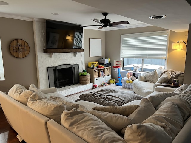 living area with visible vents, dark wood-style floors, crown molding, a brick fireplace, and ceiling fan