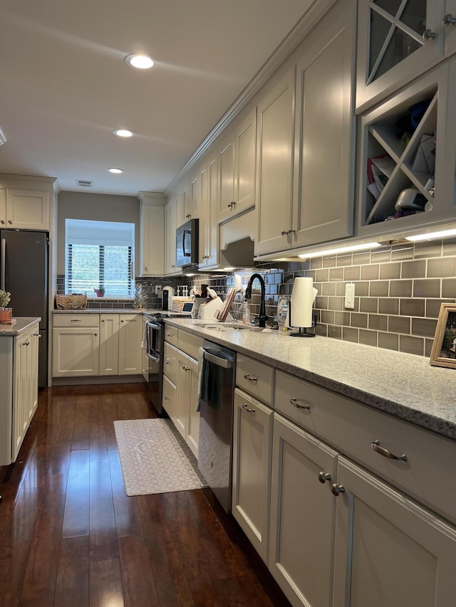 kitchen with light stone counters, backsplash, appliances with stainless steel finishes, and dark wood-style flooring