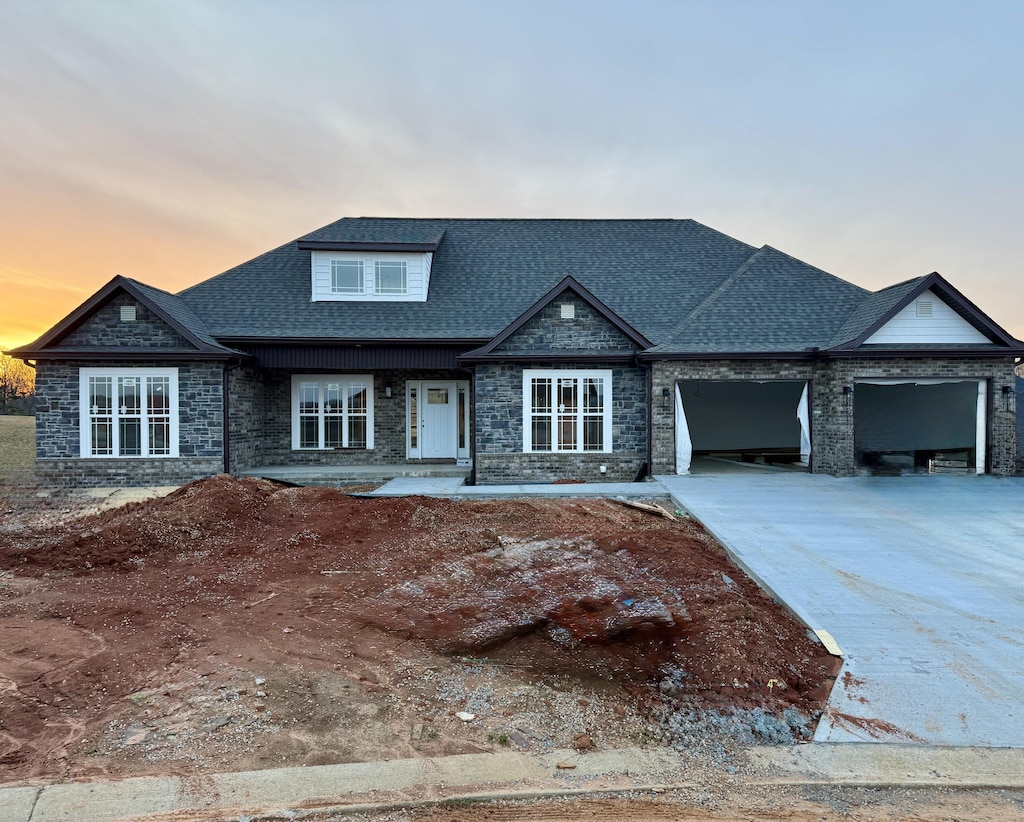 view of front of property featuring stone siding, a shingled roof, a garage, and concrete driveway