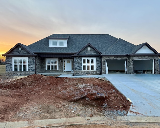 view of front of property featuring stone siding, a shingled roof, a garage, and concrete driveway