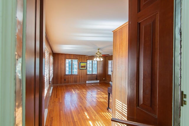 interior space featuring light wood finished floors, baseboards, baseboard heating, a ceiling fan, and wooden walls