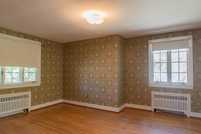 empty room with wood-type flooring, wallpapered walls, radiator heating unit, and baseboards