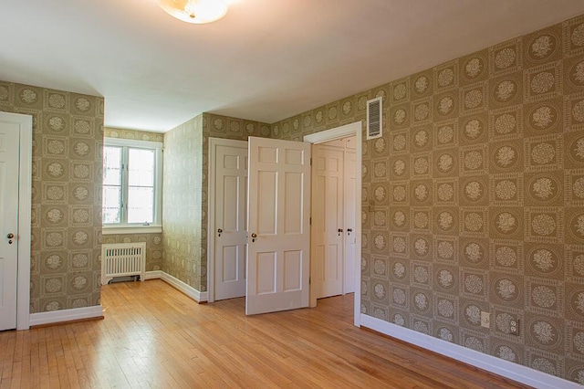 unfurnished bedroom featuring light wood finished floors, radiator, visible vents, baseboards, and wallpapered walls