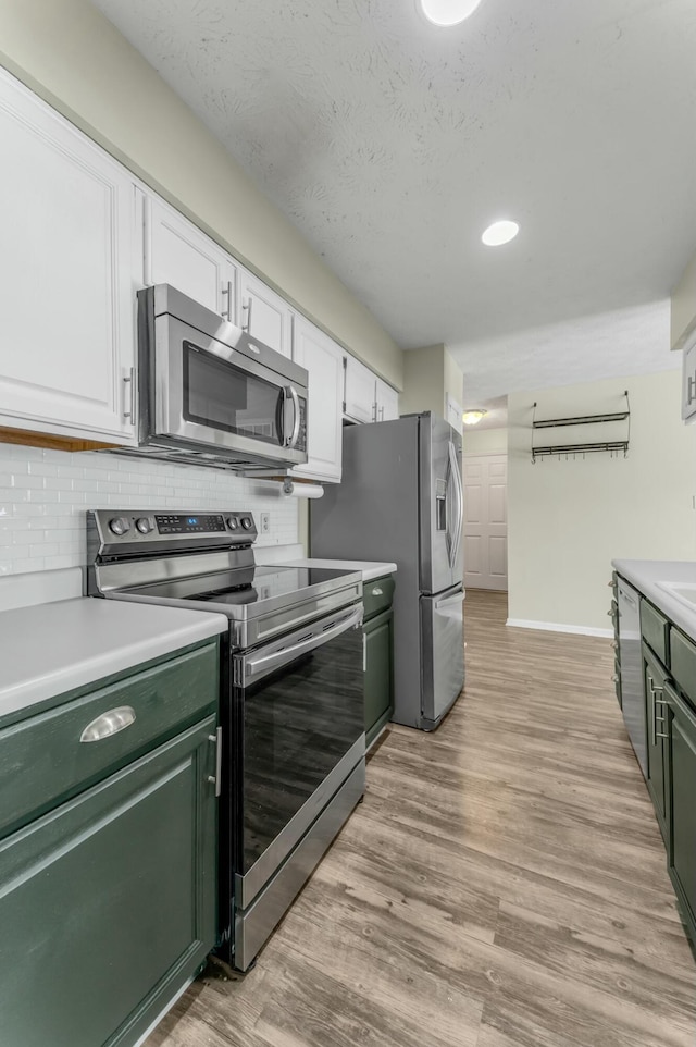 kitchen with light wood-style flooring, appliances with stainless steel finishes, green cabinets, white cabinets, and light countertops