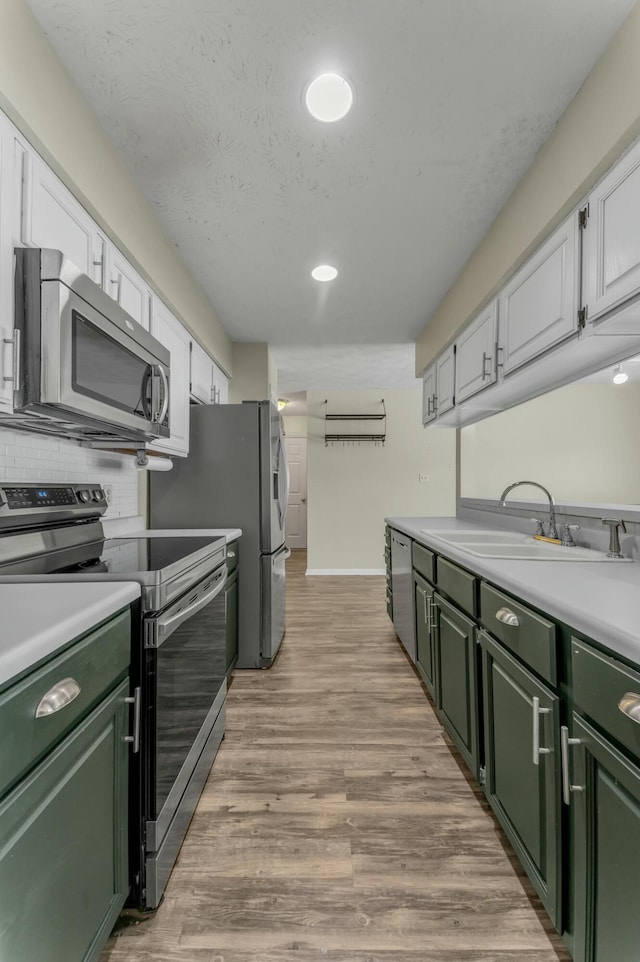 kitchen with light wood-type flooring, a sink, stainless steel appliances, green cabinets, and light countertops