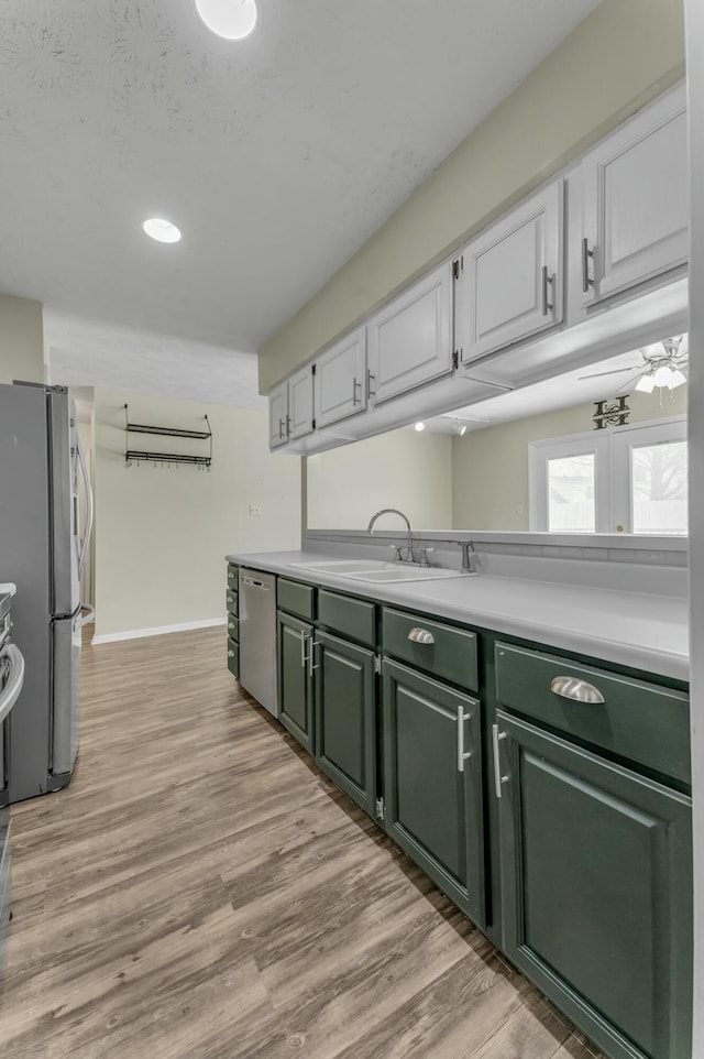 kitchen featuring green cabinetry, light countertops, light wood-style flooring, stainless steel appliances, and a sink