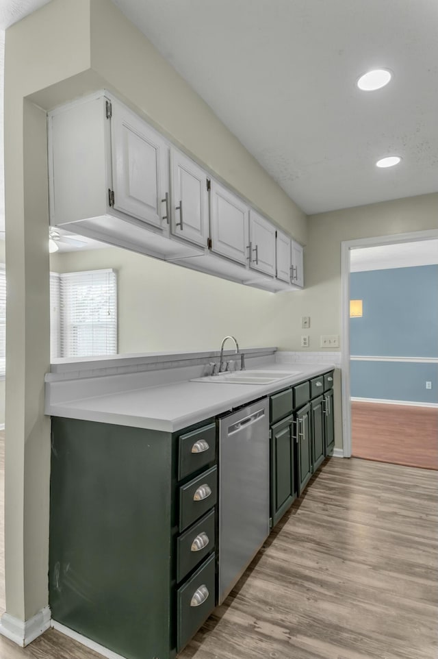 kitchen featuring light wood finished floors, dishwasher, light countertops, white cabinetry, and a sink