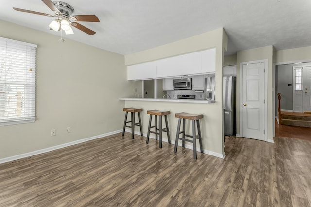 kitchen with a breakfast bar, dark wood finished floors, appliances with stainless steel finishes, white cabinets, and ceiling fan