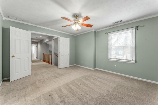 carpeted empty room with visible vents, baseboards, ceiling fan, and ornamental molding