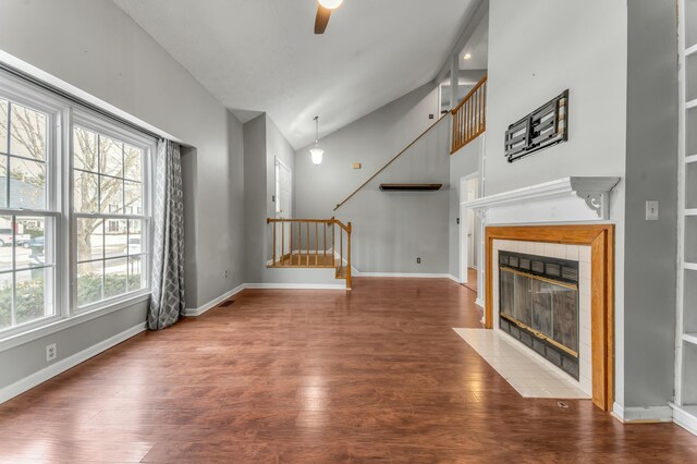 unfurnished living room with ceiling fan, wood finished floors, stairs, and a tiled fireplace