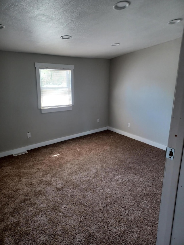 unfurnished room featuring a textured ceiling, baseboards, visible vents, and carpet