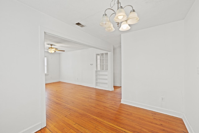 empty room featuring baseboards, light wood-style flooring, visible vents, and an inviting chandelier