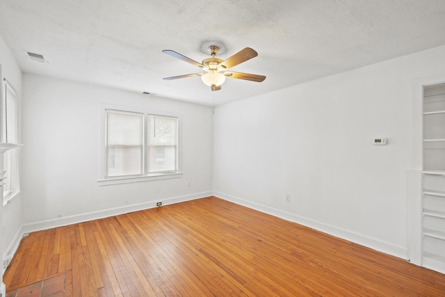 spare room featuring visible vents, light wood-type flooring, baseboards, a textured ceiling, and ceiling fan