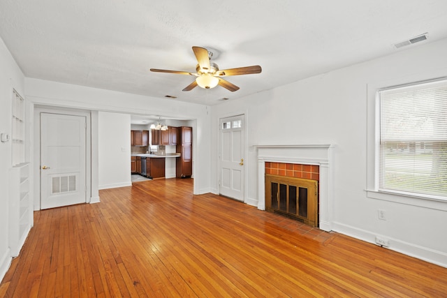 unfurnished living room with a ceiling fan, light wood-style flooring, visible vents, and a fireplace