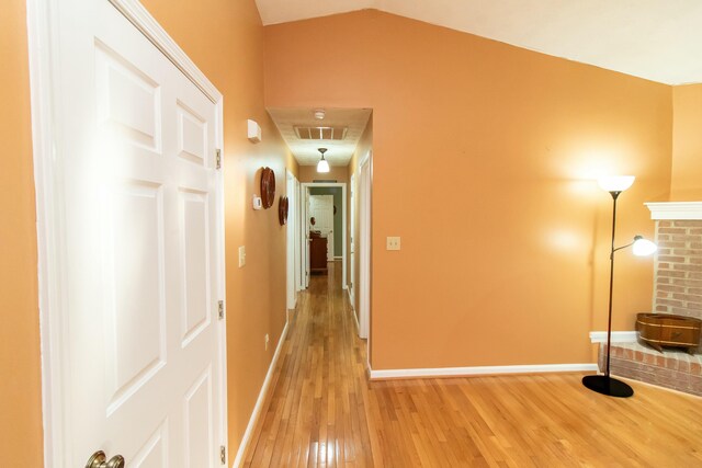 corridor with light wood finished floors, visible vents, lofted ceiling, and baseboards