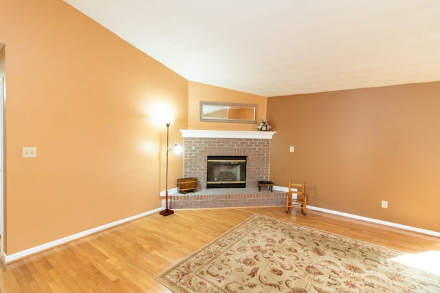 unfurnished living room featuring vaulted ceiling, a brick fireplace, baseboards, and wood finished floors