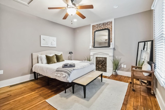 bedroom with a brick fireplace, baseboards, ceiling fan, and wood-type flooring