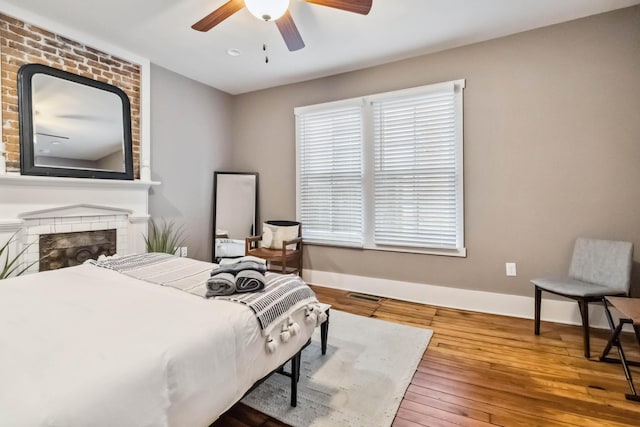 bedroom with baseboards, visible vents, a brick fireplace, and wood-type flooring