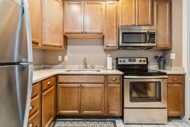 kitchen with light stone countertops, a sink, light tile patterned floors, and appliances with stainless steel finishes