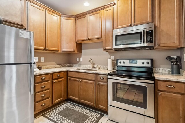 kitchen with light stone countertops, a sink, stainless steel appliances, and light tile patterned floors