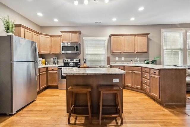 kitchen featuring a peninsula, a kitchen island, appliances with stainless steel finishes, light wood-type flooring, and a breakfast bar area