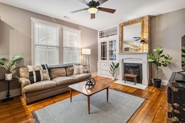 living area featuring hardwood / wood-style floors, a ceiling fan, a fireplace, and visible vents