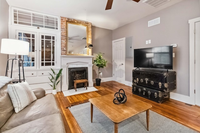 living area with wood finished floors, a brick fireplace, ceiling fan, and visible vents