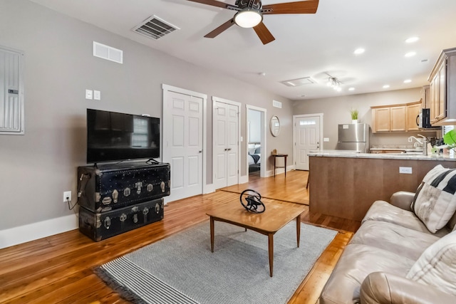 living room featuring baseboards, ceiling fan, visible vents, and light wood finished floors