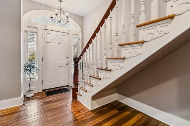 foyer with baseboards, an inviting chandelier, stairway, and hardwood / wood-style flooring