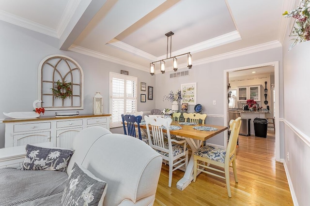 dining space featuring light wood-type flooring, visible vents, ornamental molding, a tray ceiling, and baseboards