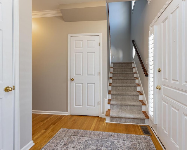 staircase featuring visible vents, crown molding, baseboards, and wood finished floors