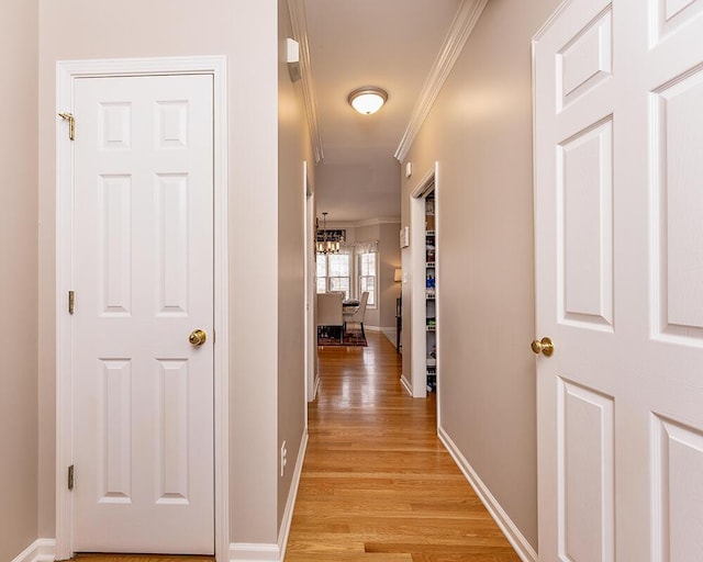 hall featuring a notable chandelier, baseboards, crown molding, and light wood-style floors