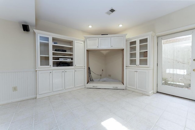 interior space with visible vents, white cabinetry, glass insert cabinets, and a wainscoted wall