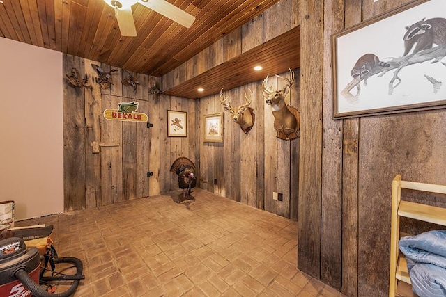 interior space featuring wooden walls, wood ceiling, brick floor, and ceiling fan