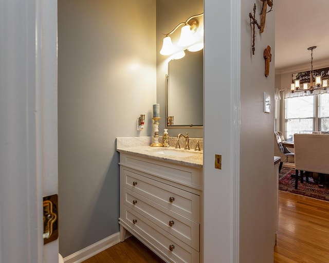 bathroom featuring baseboards, a notable chandelier, wood finished floors, and vanity