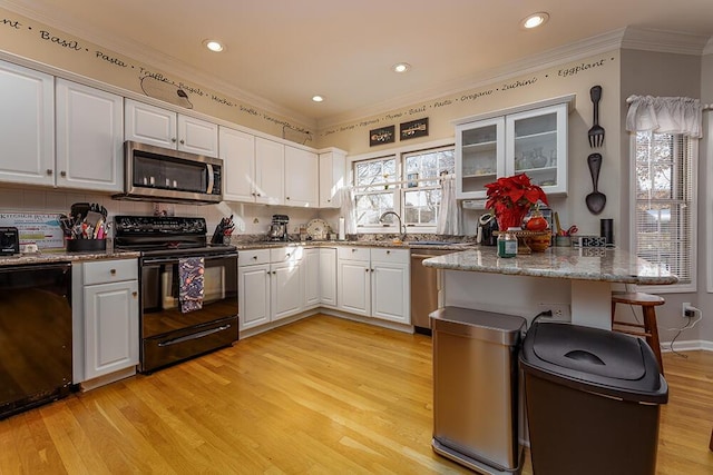 kitchen featuring a peninsula, light wood-style flooring, black appliances, white cabinets, and crown molding