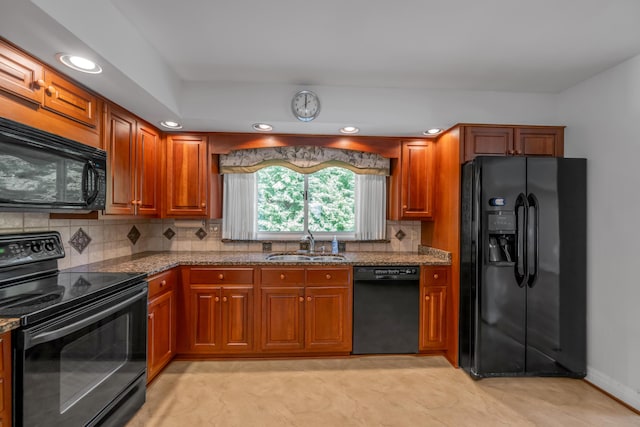 kitchen with brown cabinets, black appliances, a sink, dark stone counters, and decorative backsplash