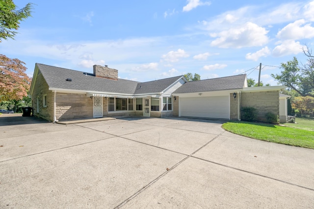 view of front of house featuring brick siding, concrete driveway, a front yard, a chimney, and an attached garage