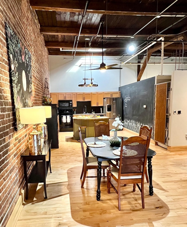 dining space featuring light wood finished floors, brick wall, beamed ceiling, a towering ceiling, and a ceiling fan