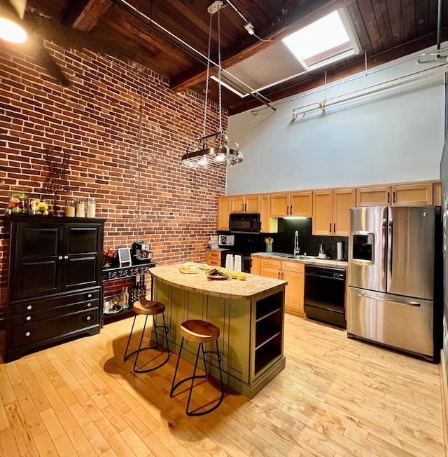 kitchen with light brown cabinets, brick wall, black appliances, a towering ceiling, and a center island