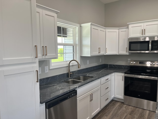 kitchen with white cabinets, dark stone counters, stainless steel appliances, and a sink