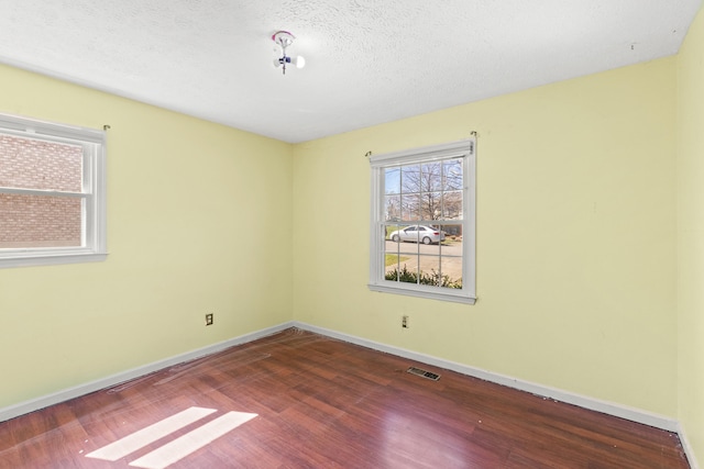 empty room with baseboards, wood finished floors, visible vents, and a textured ceiling