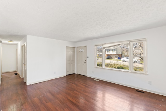 unfurnished living room featuring visible vents, baseboards, dark wood-style floors, and a textured ceiling