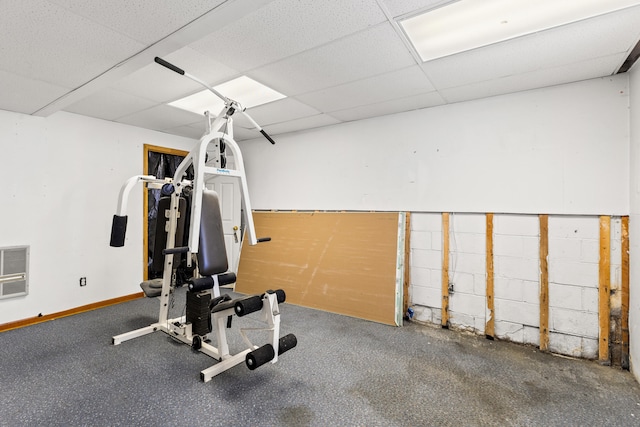 workout area featuring a paneled ceiling and baseboards