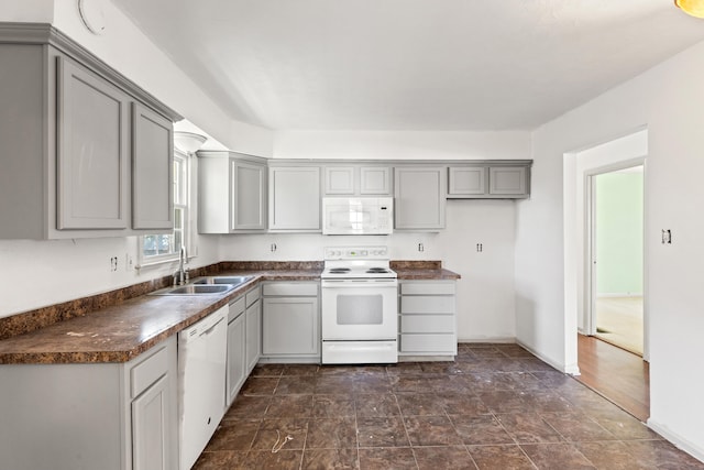 kitchen with dark countertops, a sink, white appliances, stone finish floor, and gray cabinetry