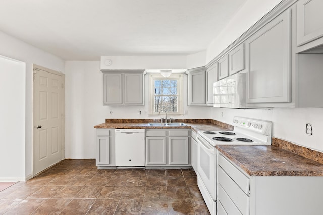 kitchen with dark countertops, gray cabinetry, a sink, and white appliances