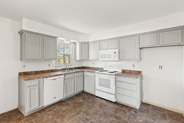 kitchen with dark countertops, gray cabinetry, a sink, and white appliances