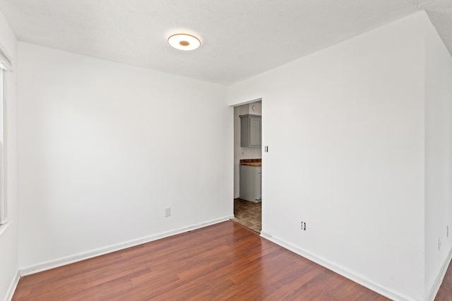 unfurnished room with baseboards and dark wood-type flooring